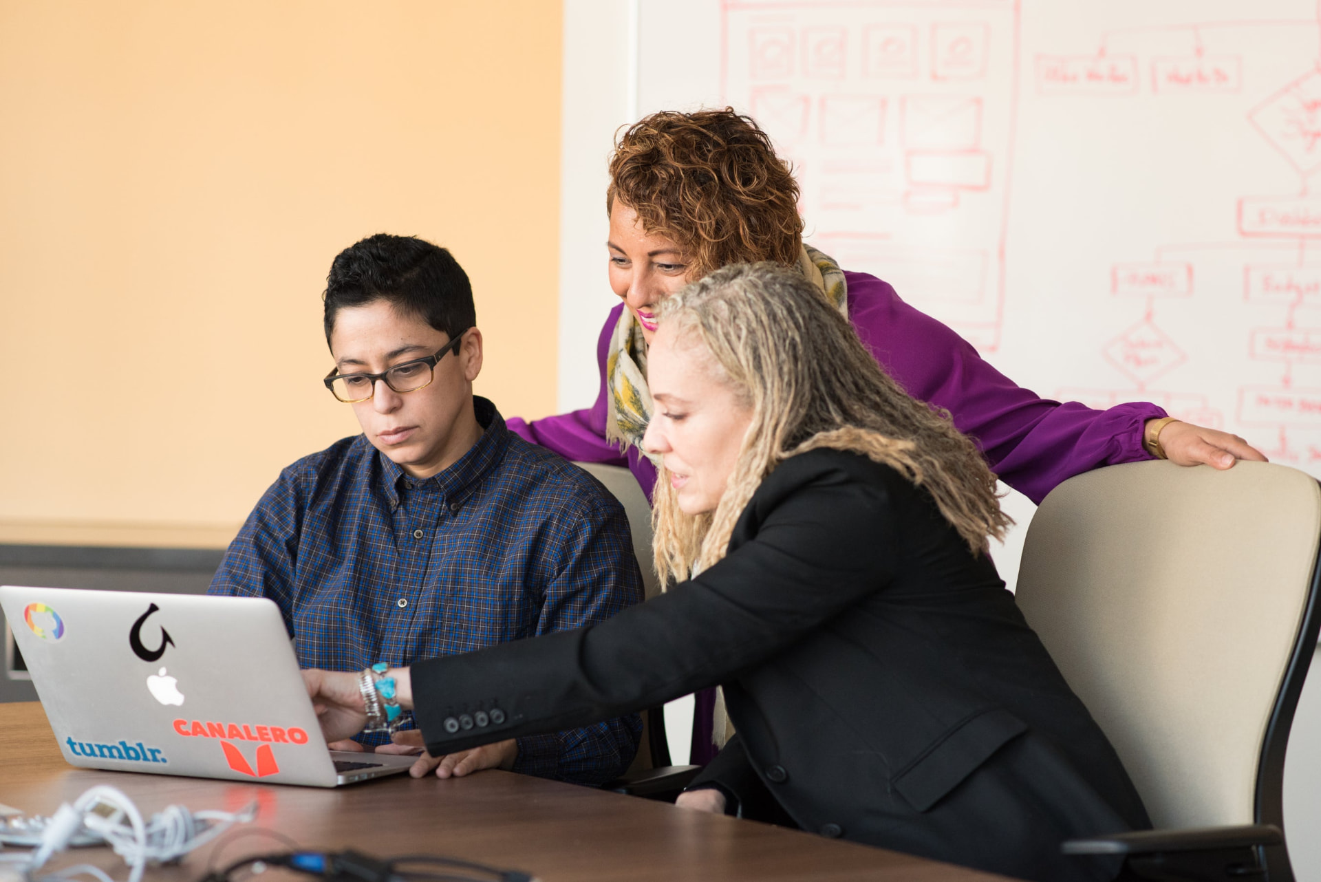 Three educators collaborating around a laptop in a meeting room