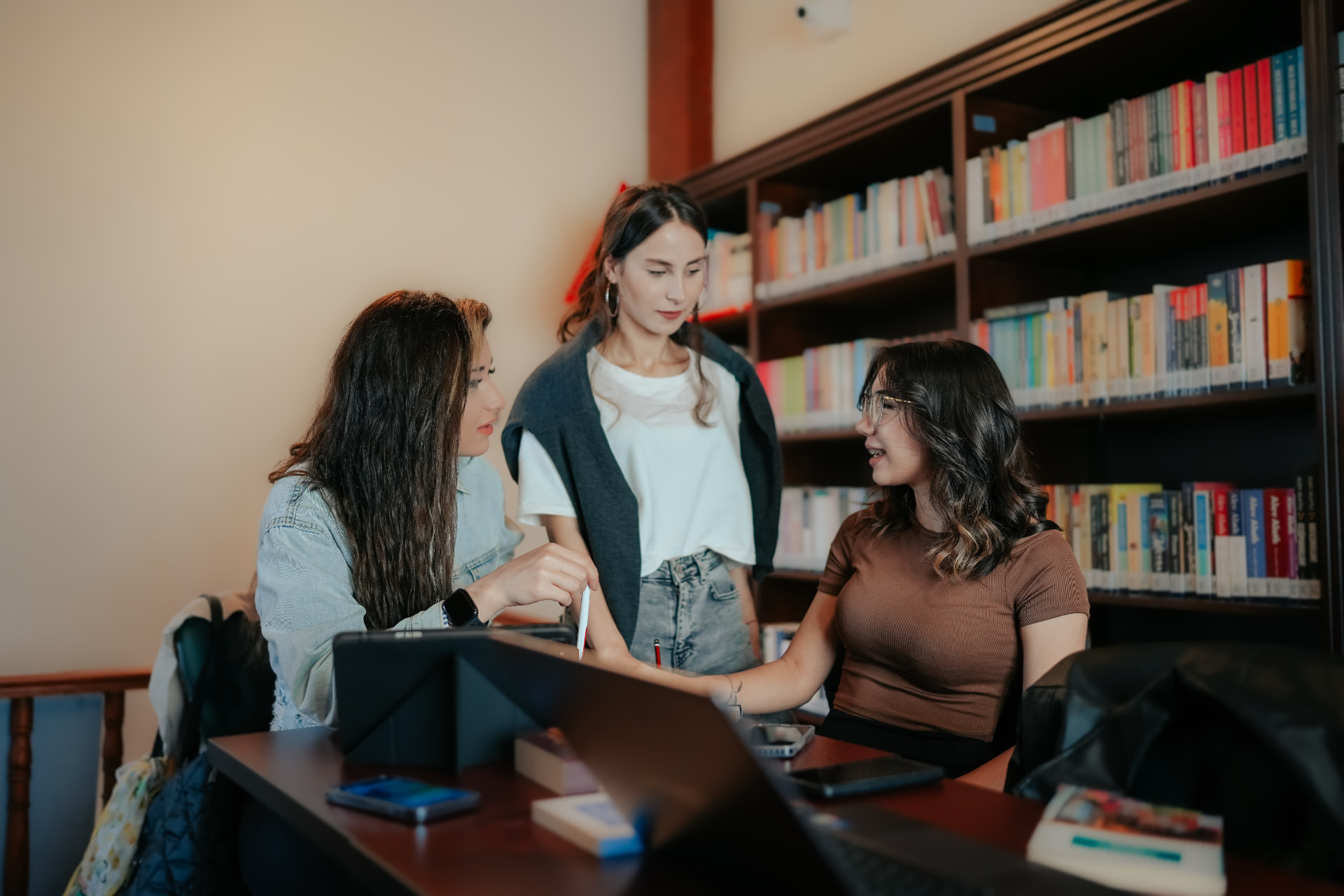 Three students collaborating around a laptop in a library